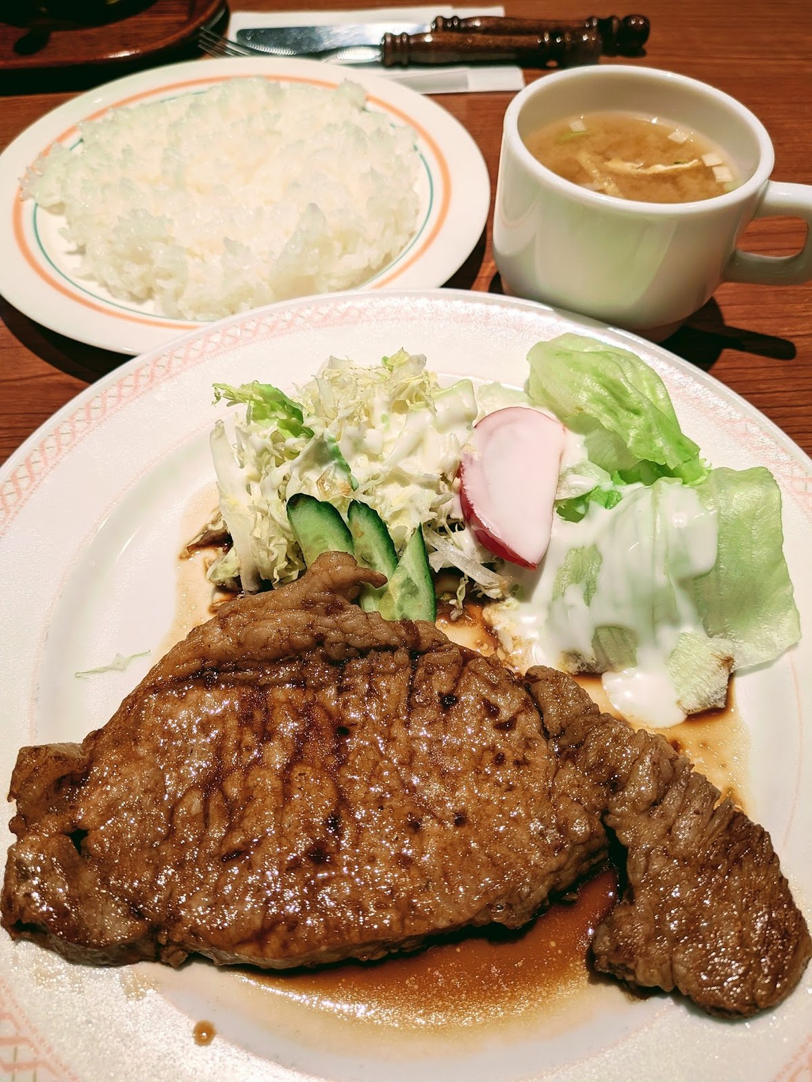 大皿に盛られた生姜焼きとサラダ、奥に白いライス皿とスープカップが並ぶ定食