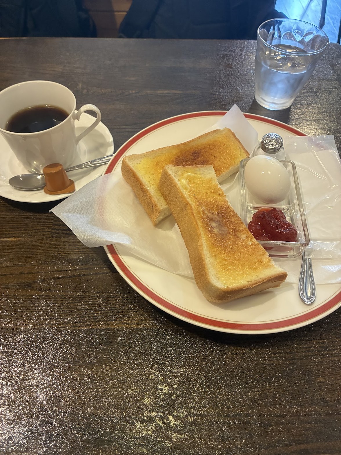 赤縁の白皿にトースト2枚とゆで卵・ジャム、左隣に白磁カップのブラックコーヒーが並ぶモーニングセット